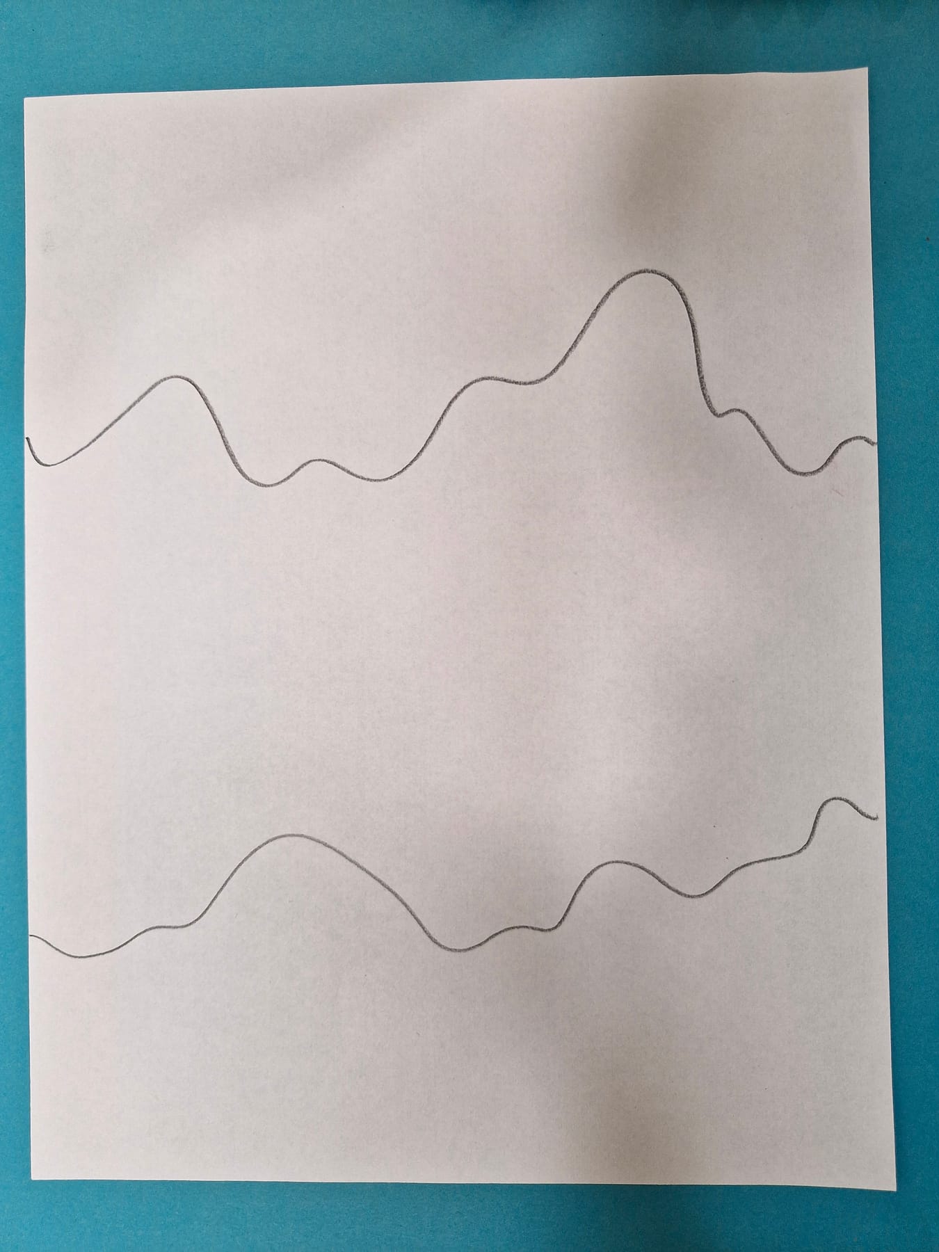 A sheet of white paper with two long wavy pencil lines drawn across it from one side to the other.