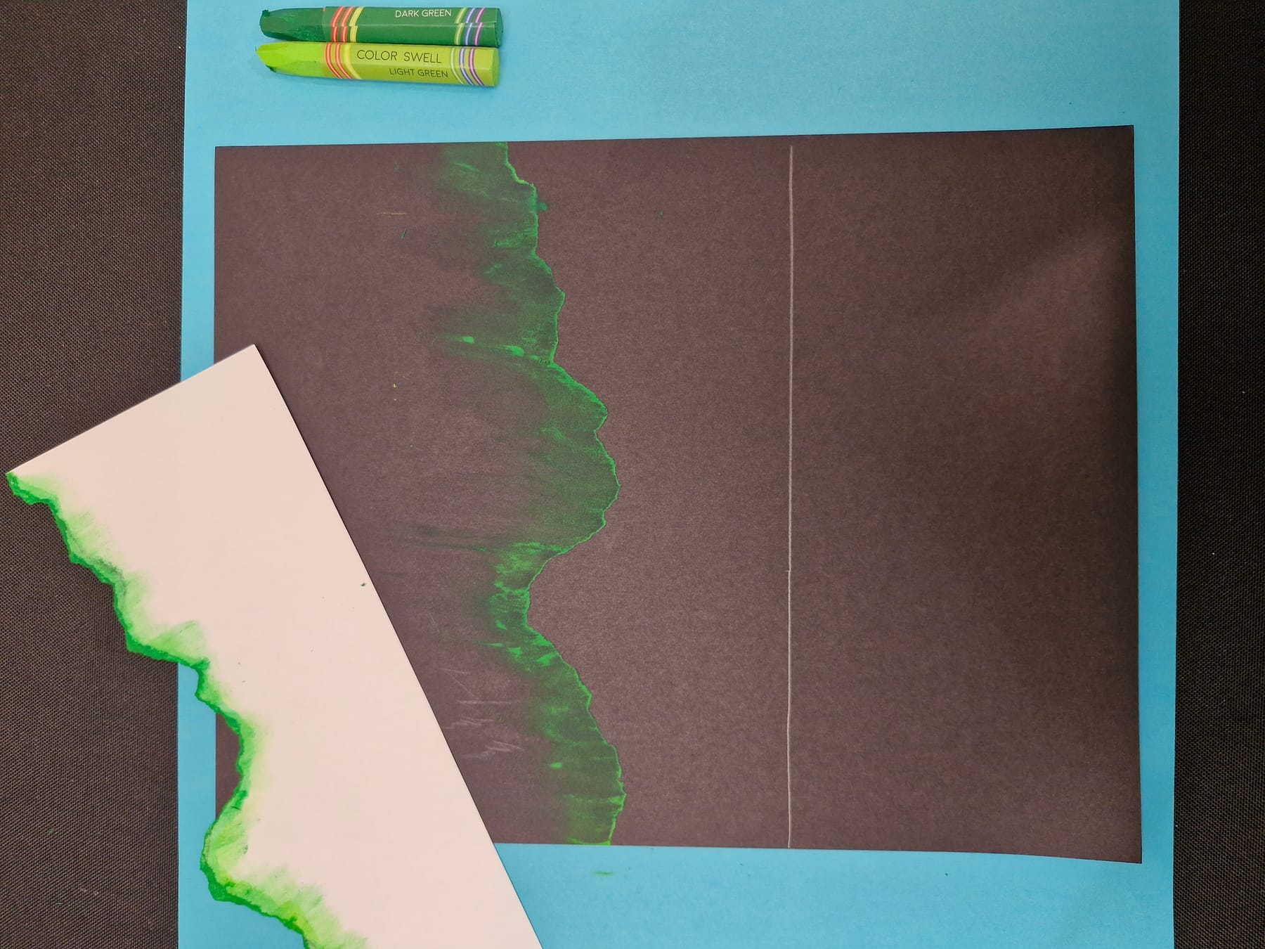 The torn paper lifted straight up, leaving a band of green light that is sharp on one side and fades into the dark on the other.