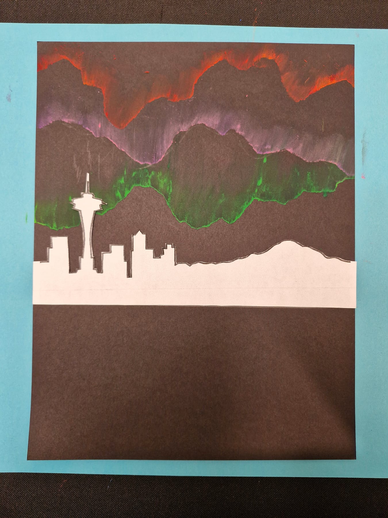 The skyline laid along the horizon, its dark buildings silhouetted against the green and purple light above.