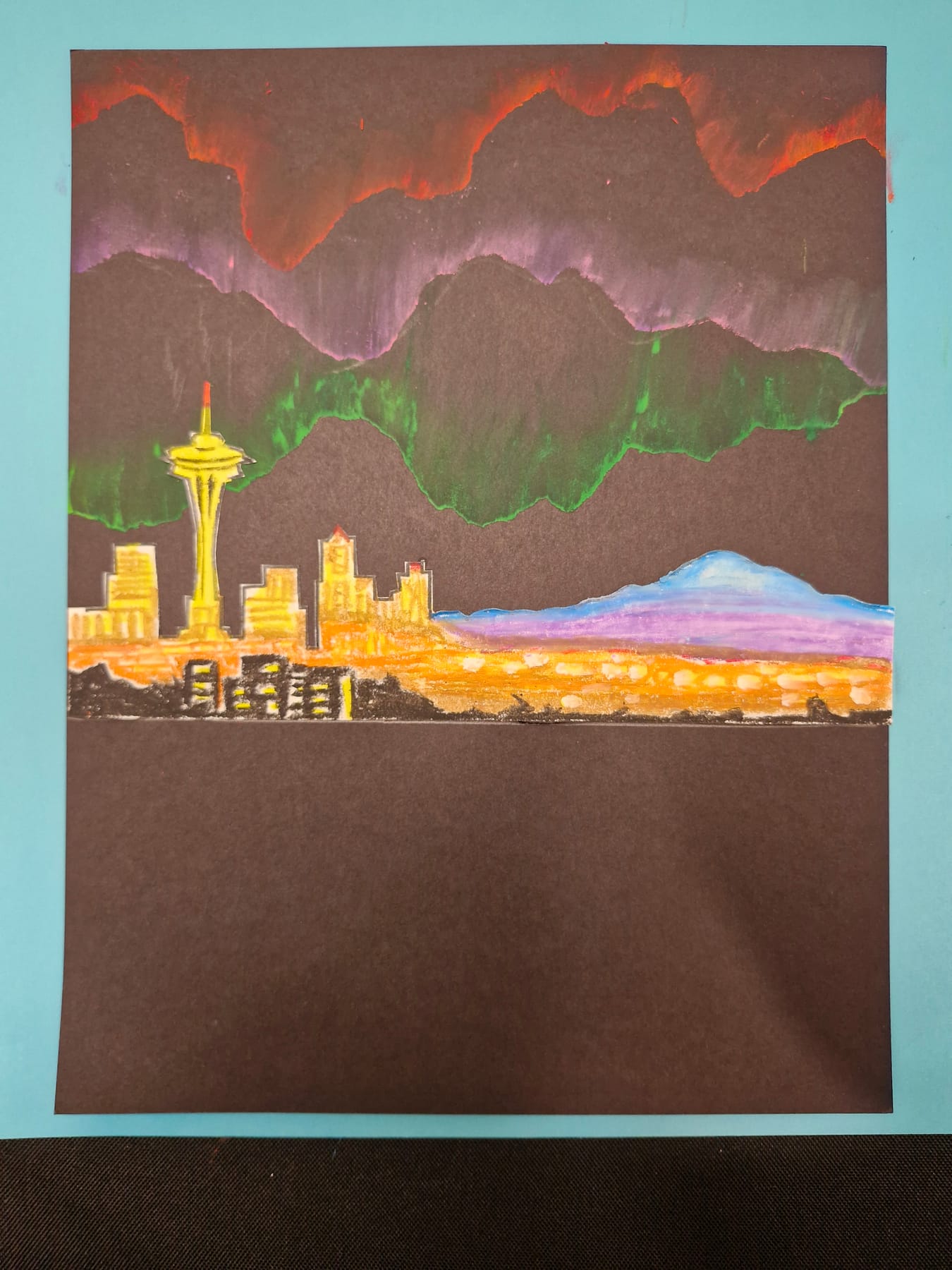 The city glued down, its windows and street lights drawn in gold, with Mount Rainier added in pale blue behind it.