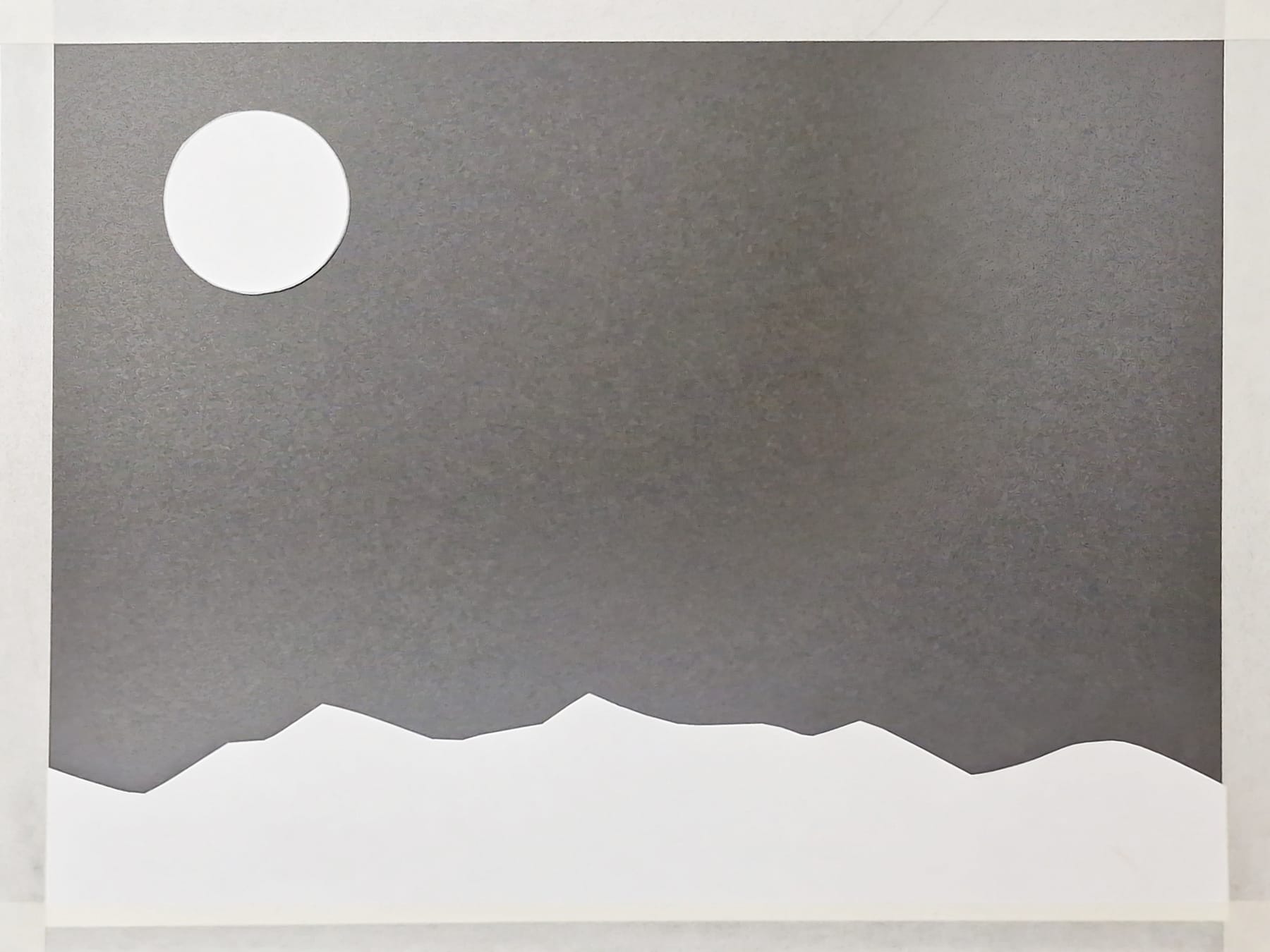 The cut white circle and the cut mountain ridge laid in position on dark paper, before any color has been added.