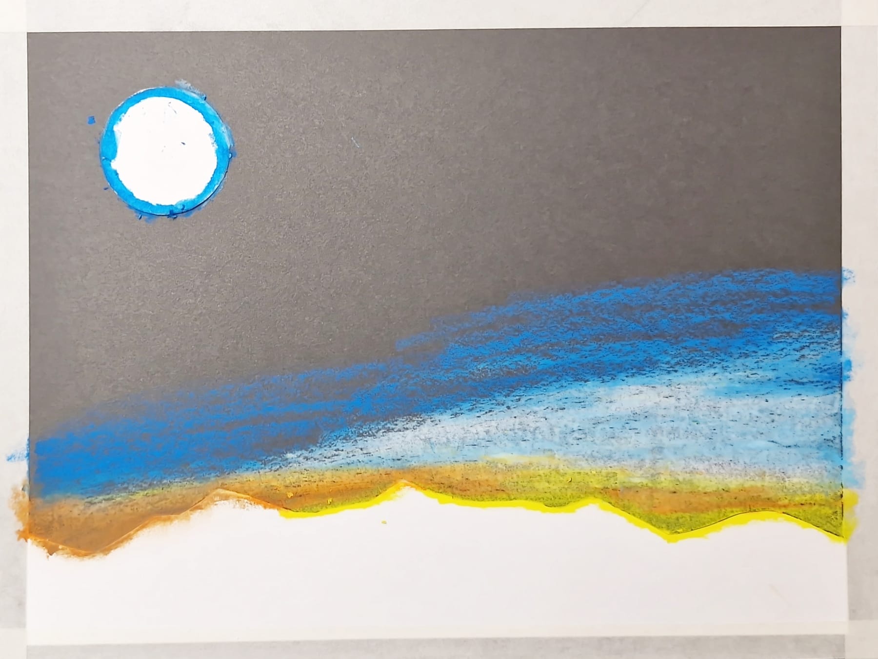 The mountain stencil held down while yellow, orange and blue are rubbed upward off its jagged edge into a sunset sky, the white circle still in place above.