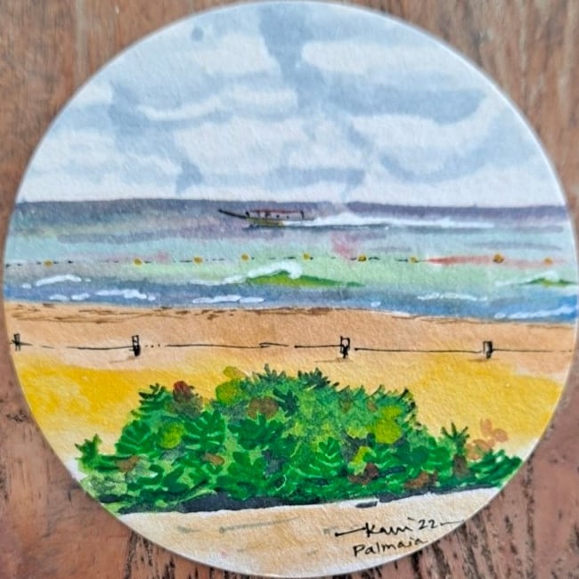 Ayesa Kaur’s small round watercolor of a beach: green dune plants on golden sand, a fence line, and a blue sea under gray clouds